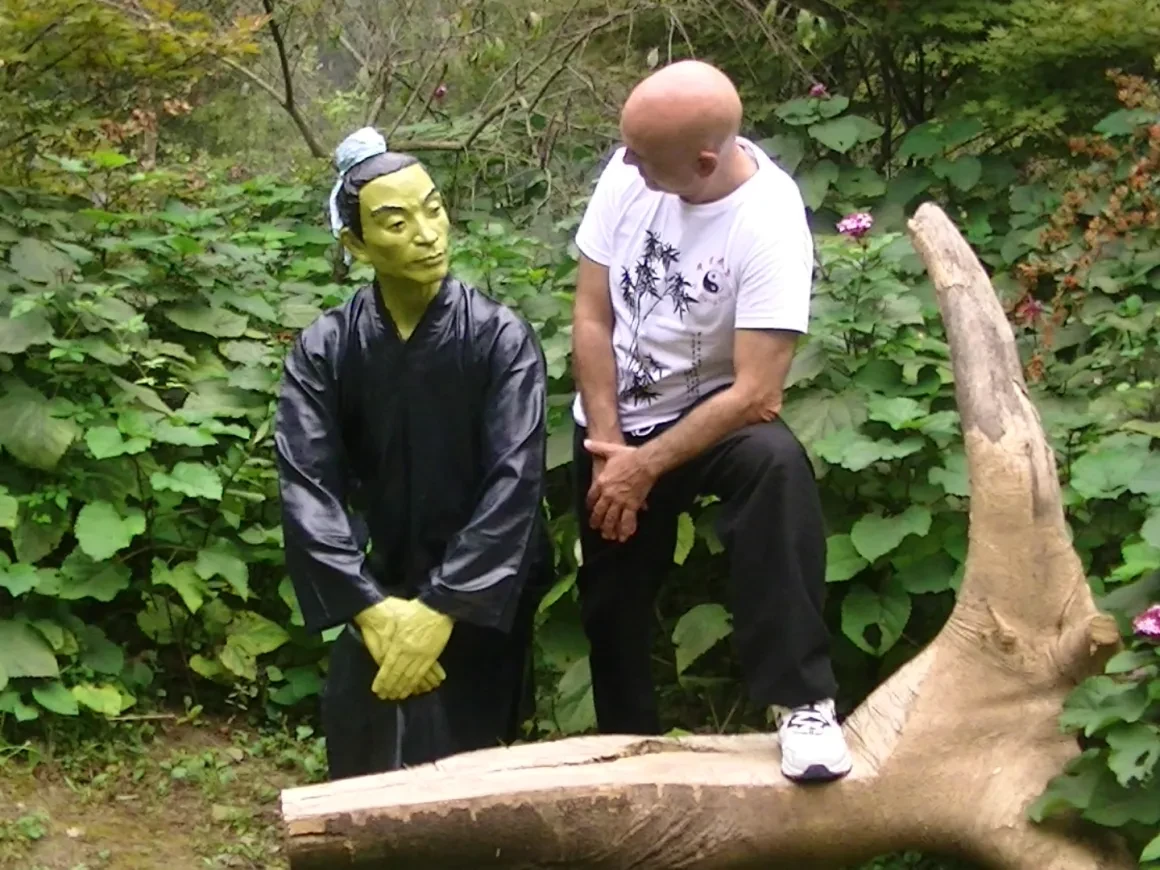 Tony Garcia seated beside a traditional figure sculpture on a log