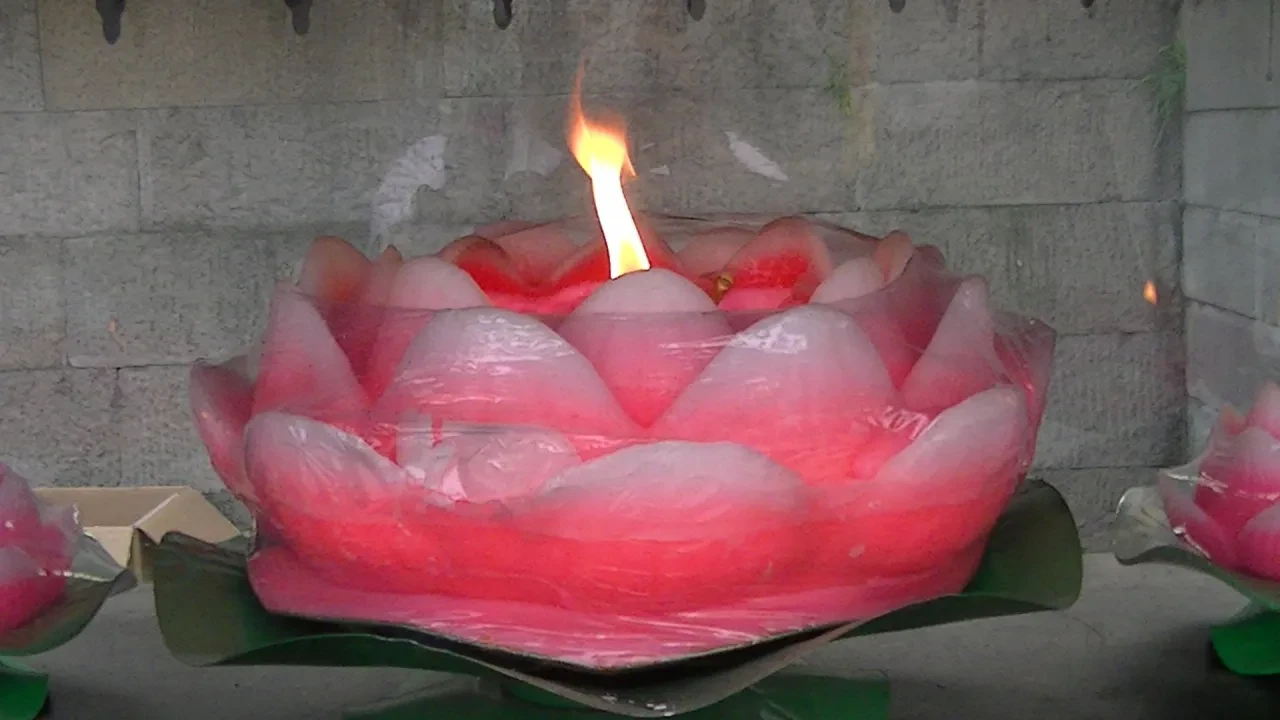Lotus-shaped ceremonial candle burning at a temple shrine