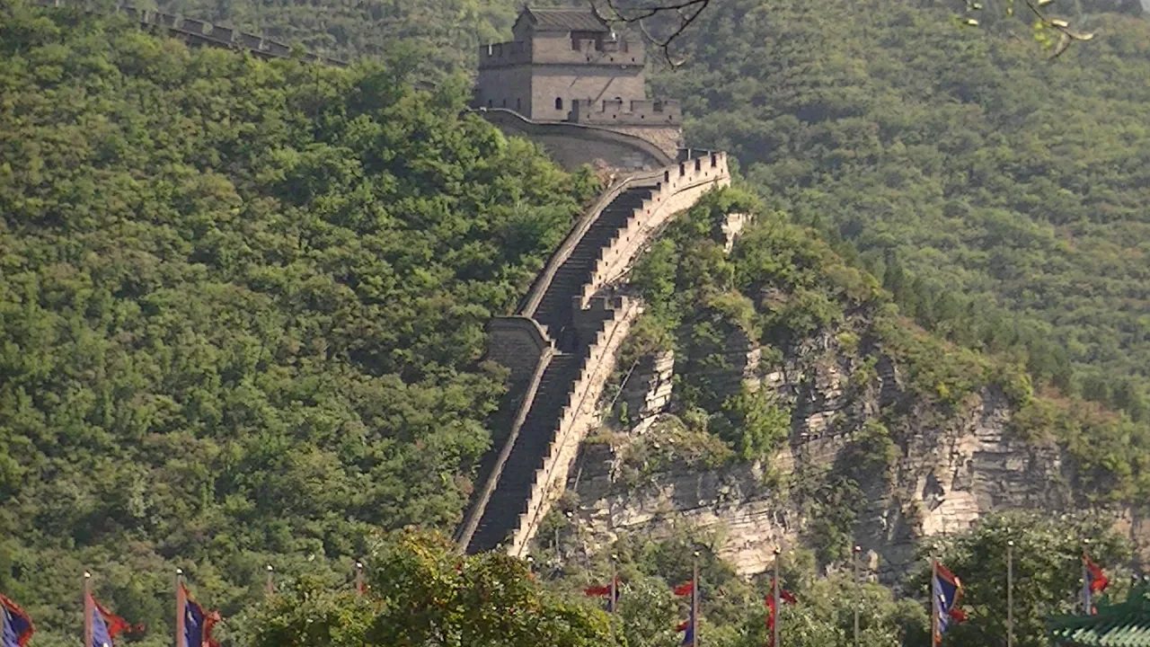 The Great Wall climbing steeply over a rocky ridge with colorful flags below