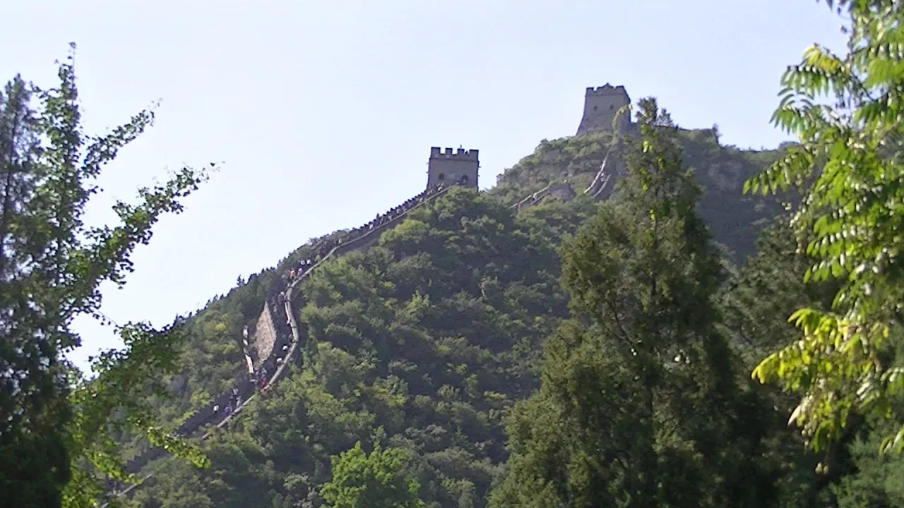 The Great Wall climbing a steep forested ridge with two watchtowers visible